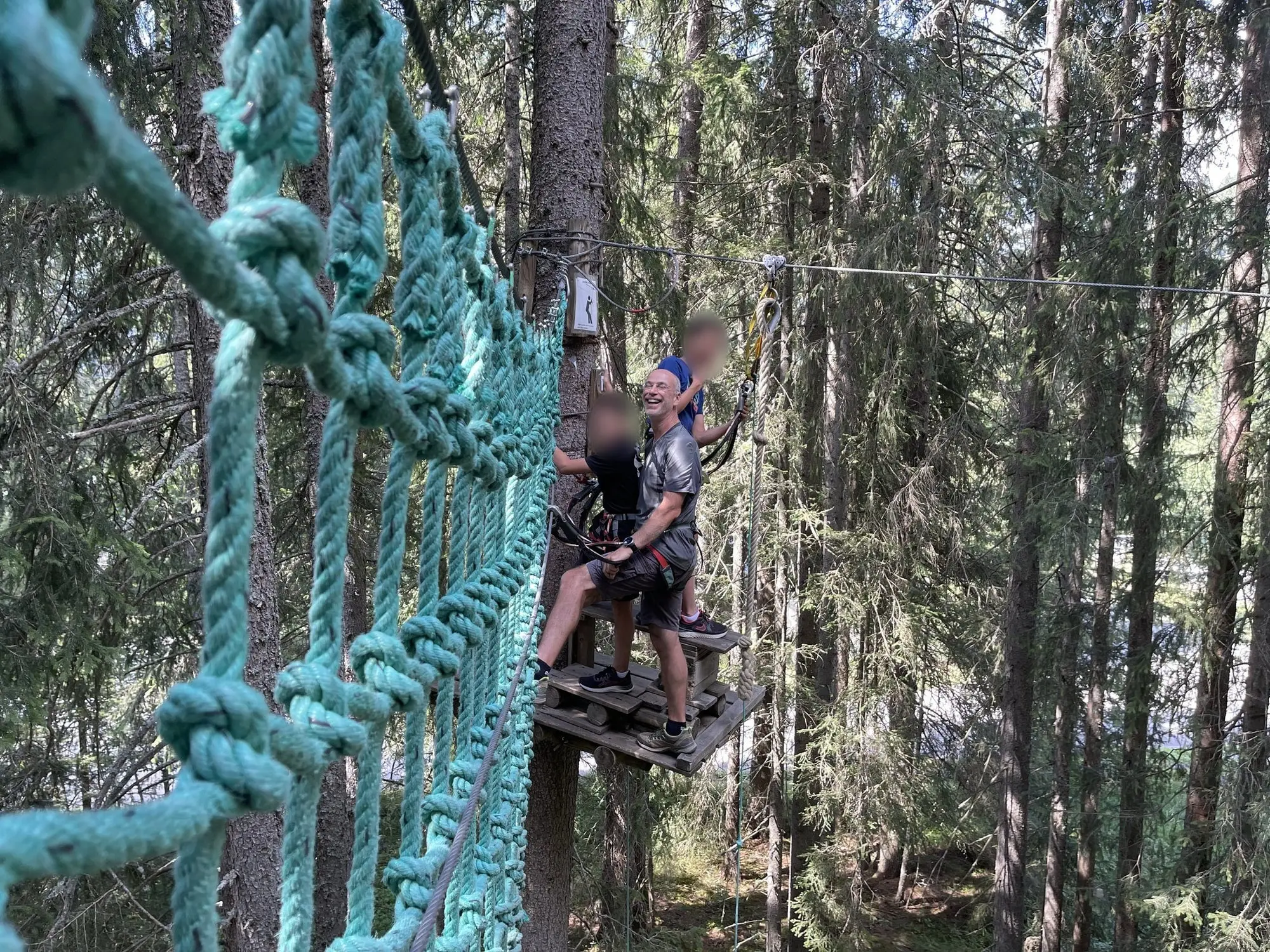 En famille dans un parc accrobranche, sur une plateforme entre les sapins