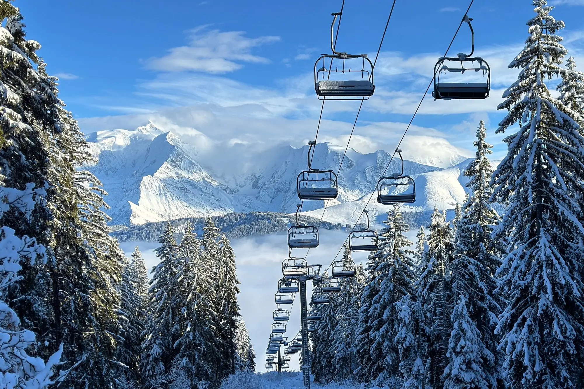 Ein Sessellift über verschneiten Tannen, in der Ferne das Mont-Blanc-Massiv