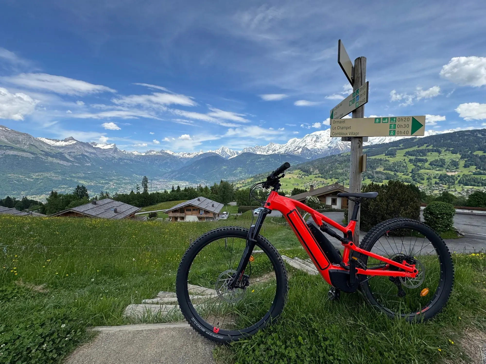 Un VTT électrique devant un panneau de sentier, le massif du Mont-Blanc au fond