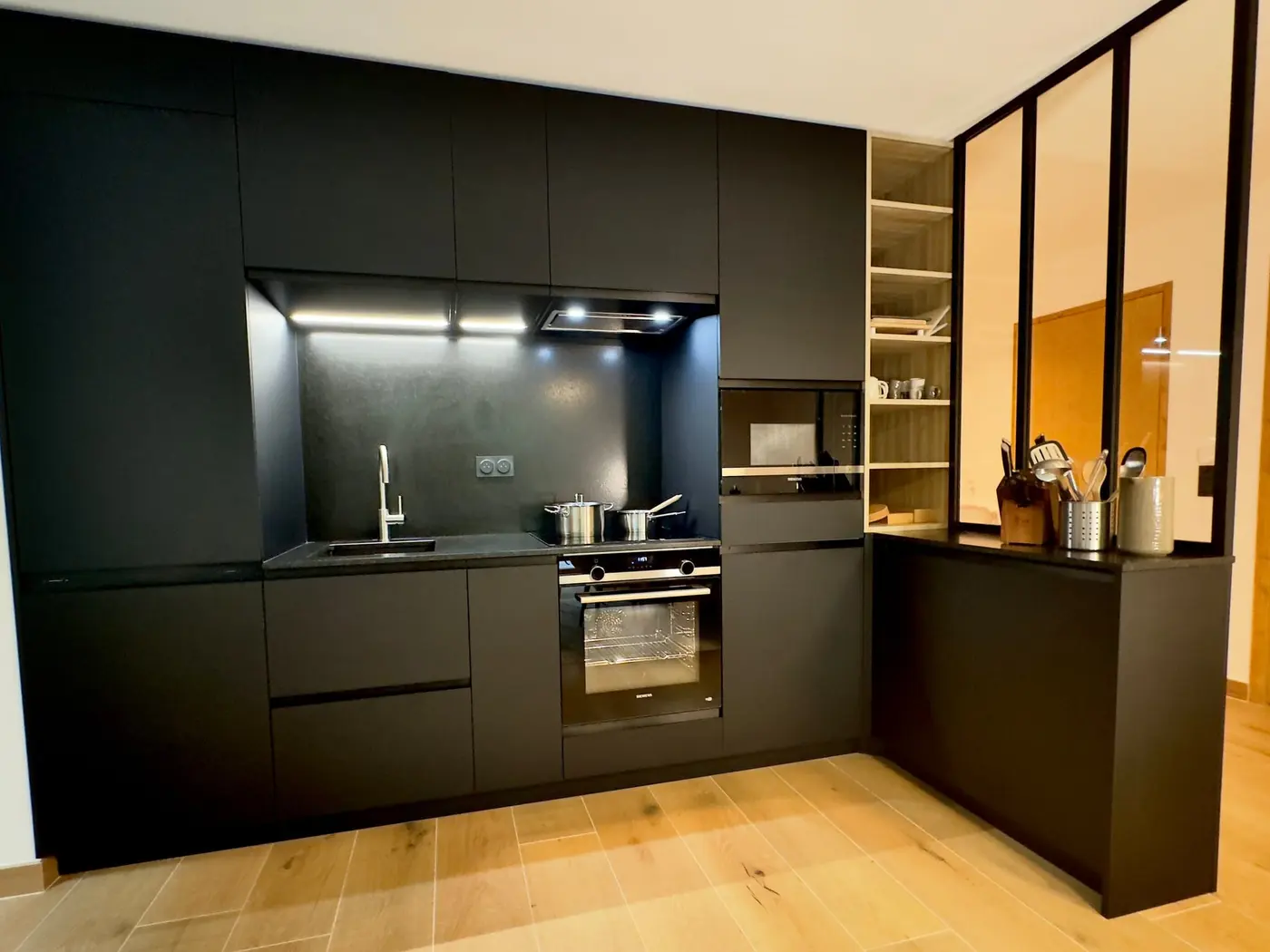 La cuisine : façades noires, four, plaque et verrière