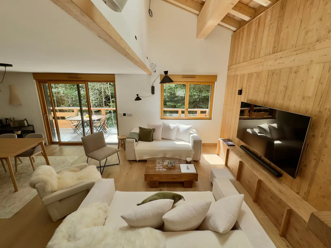 La pièce de vie du duplex sous la charpente : salon, poutres et baies sur la forêt